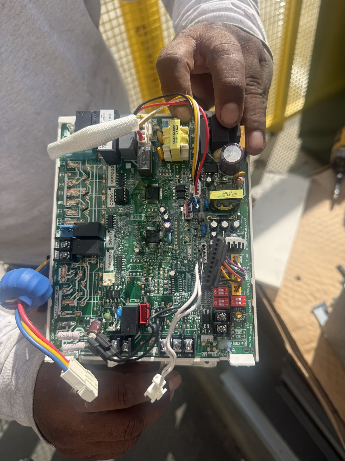 Technician holding an HVAC indoor unit main control board with wiring harnesses attached.