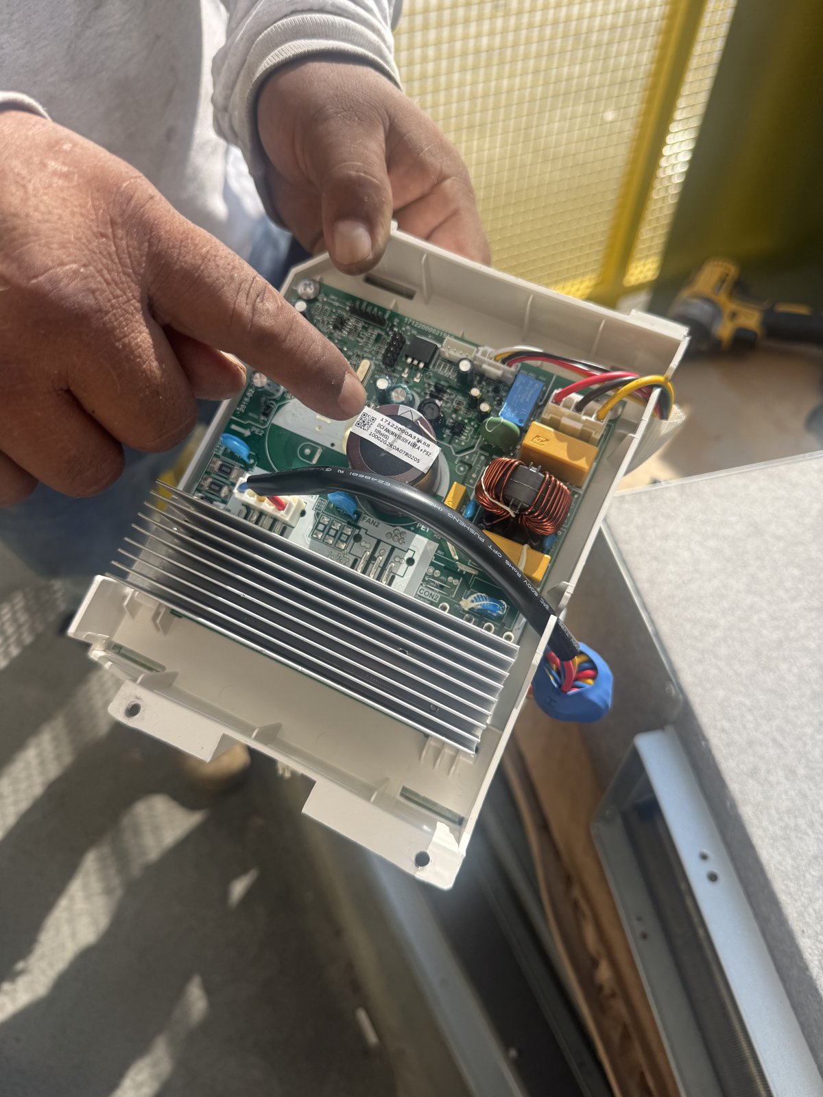 Technician pointing at an HVAC inverter drive board with an aluminum heat sink.